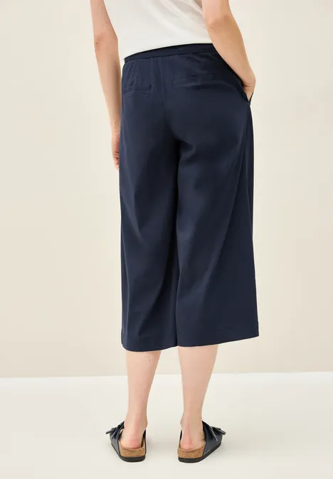 Frau trägt dunkelblaue Culotte und weiße Bluse, von hinten fotografiert.